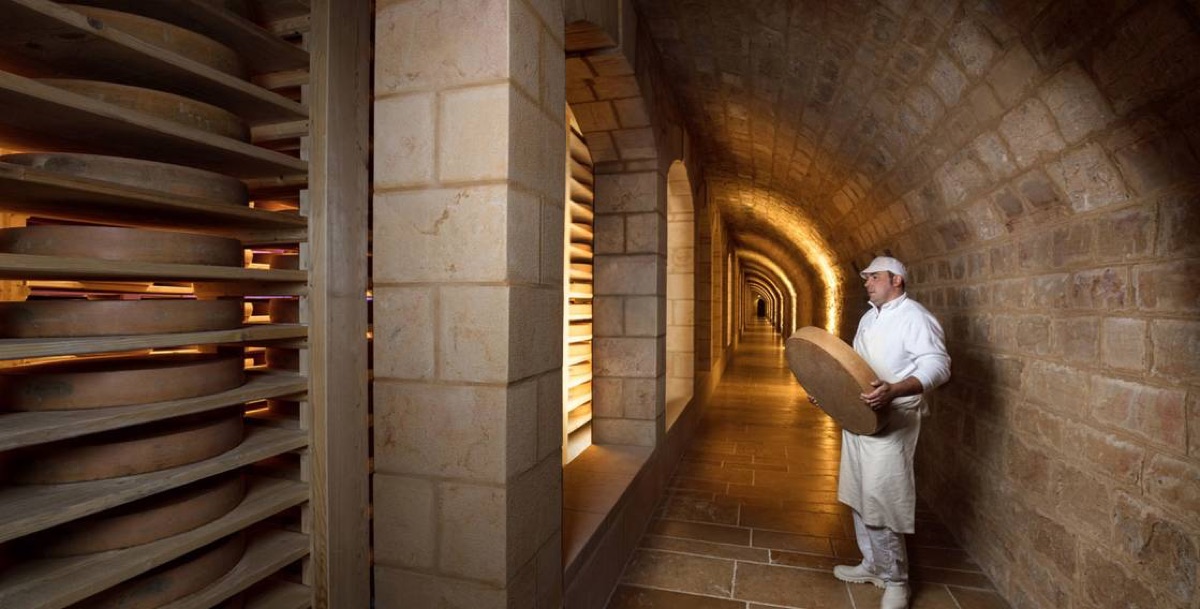 Affineur trägt einen Comté-Laib durch ein Kellergewölbe im Fort des Rousses