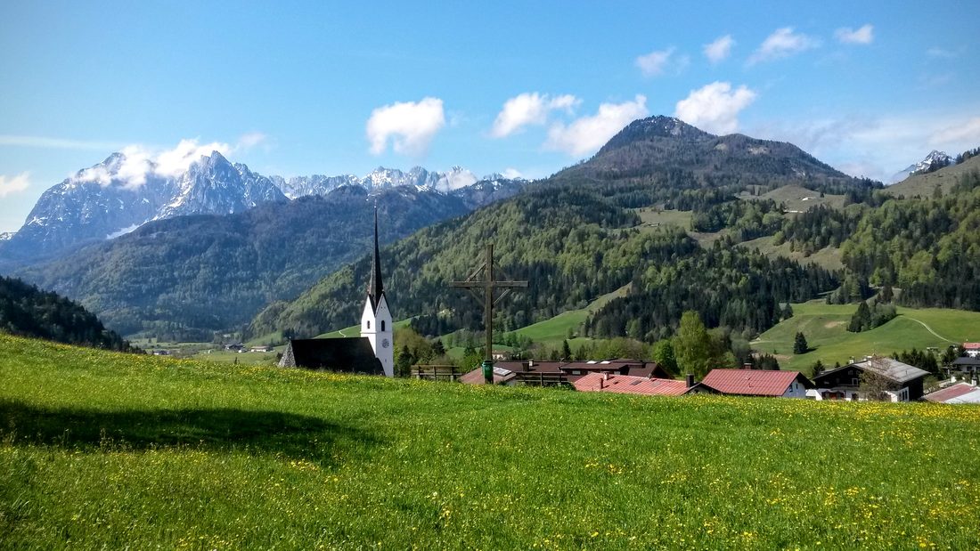 Das Dorf Schwendt mit Kirche und Wiesen, dahinter der schneebedeckte Wilde Kaiser